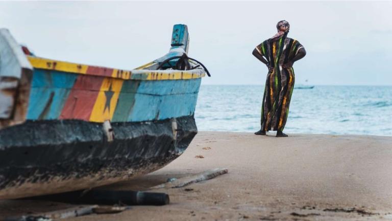 A man standing next to a boat on the beach.