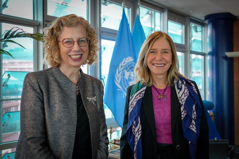 Two women standing next to each other in front of flags.