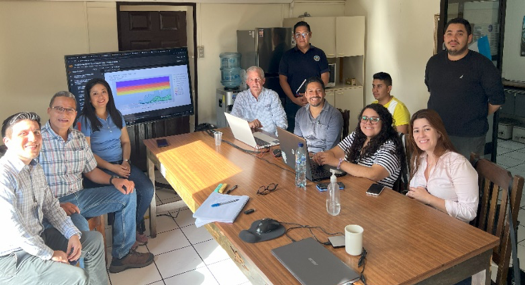 A group of professionals gathered around a table during a meeting with a presentation on the computer screen.