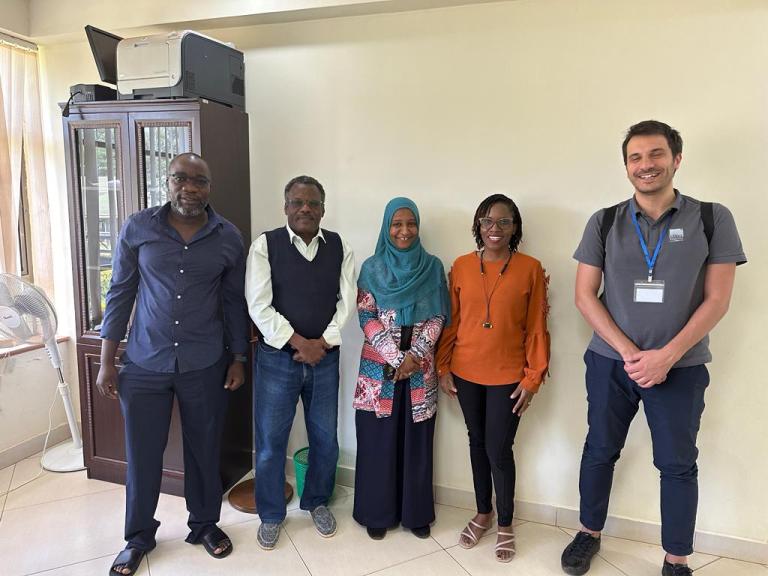 Group of five professionals posing for a photo in an office setting.