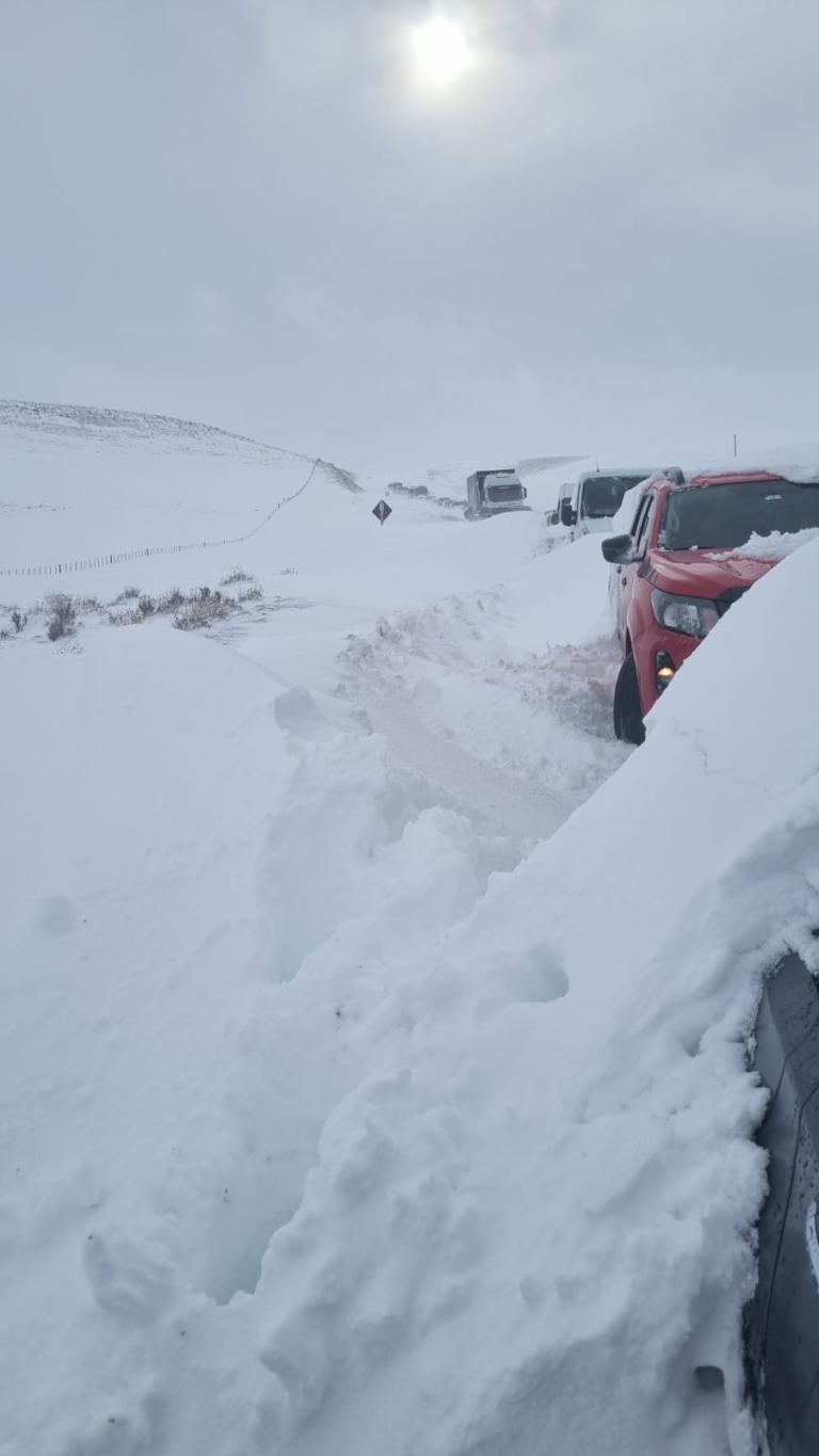 Argentina - Vehicles stuck on a snow-covered road, sun barely visible through cloud cover.