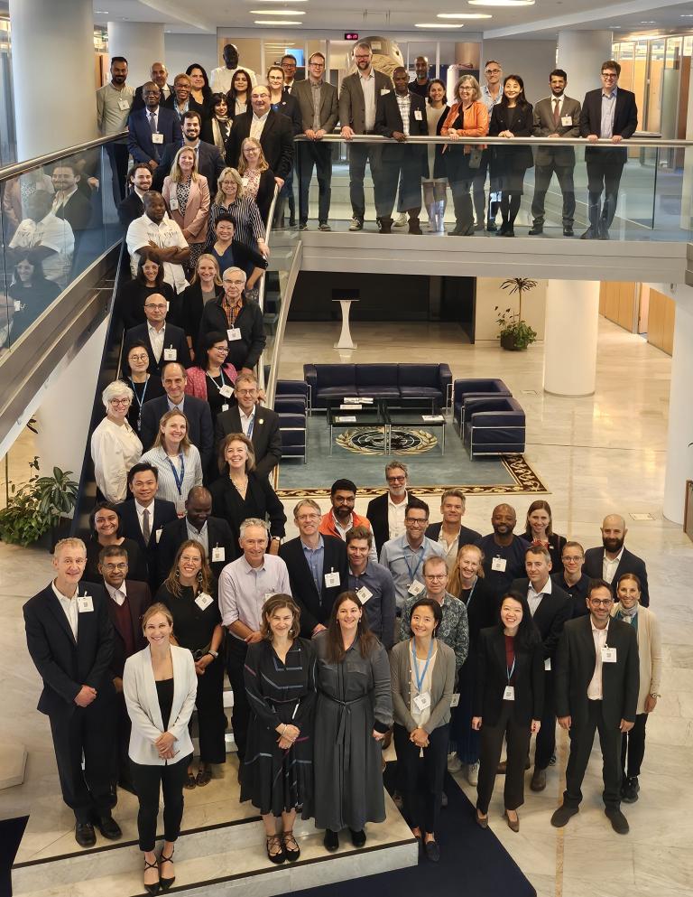 A large group of professionals stands on a staircase and in a lobby area inside a modern building, posing for a group photo.