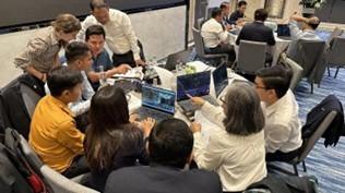 A group of people sit around a table with laptops, engaged in discussion.