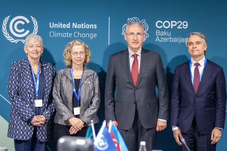 Four individuals stand in front of a COP29 Baku Azerbaijan backdrop, featuring United Nations Climate Change logos. They are dressed formally and wearing conference badges.