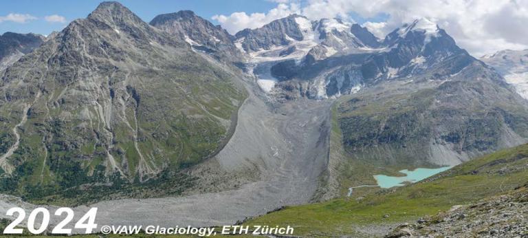 Mountain landscape with steep green slopes, rocky terrains, and a small lake. Snow-capped peaks are visible in the background. Image labeled "2024 ©VAW Glaciology, ETH Zürich".