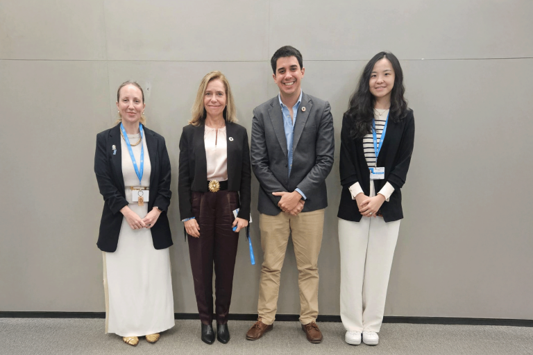 Four people stand side by side against a gray background, wearing business attire and smiling at the camera.