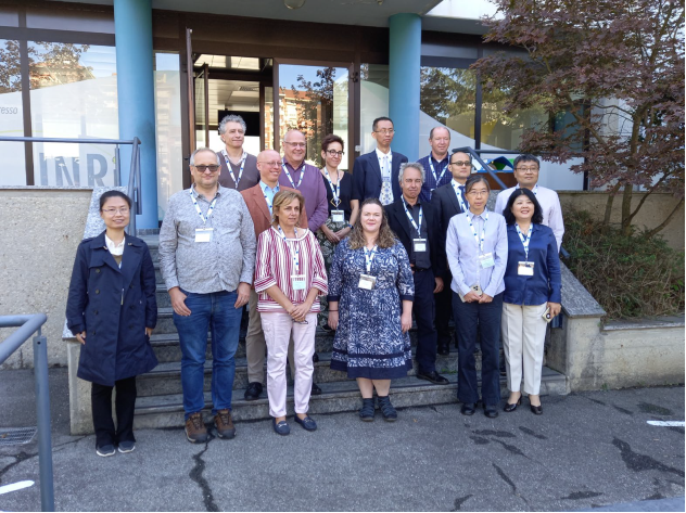 A group of fifteen people stand on steps outside a building, wearing business casual attire and conference badges.