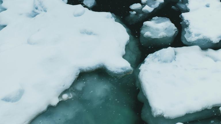 Chunks of snow-covered ice floating on dark green water.