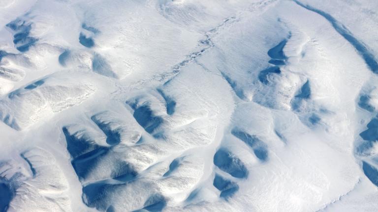 Aerial view of snow-covered mountainous terrain with deep ridges and shadowed valleys.