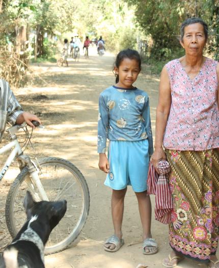 A group of people standing next to a bicycle on a dirt road.