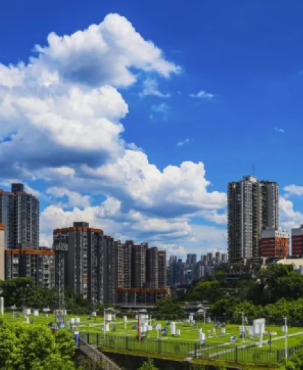 Urban skyline with tall residential buildings, green spaces, and a cemetery in the foreground under a partly cloudy sky.