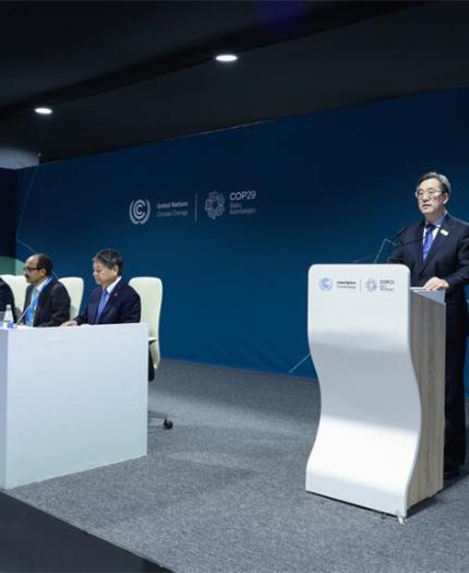 A person speaks at a podium on a stage with six seated individuals at a climate conference, featuring a blue backdrop displaying "COP28" and the UN logo.