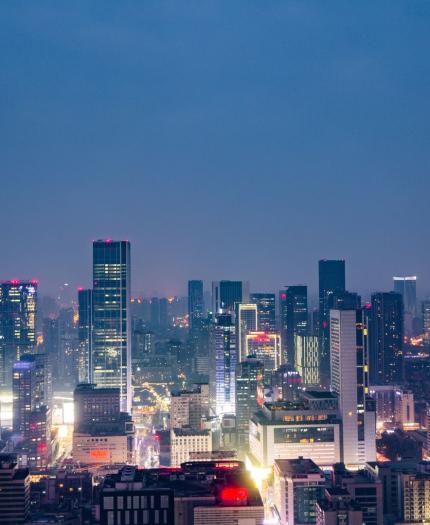 Aerial view of a city skyline at night with illuminated skyscrapers and buildings under a deep blue sky.